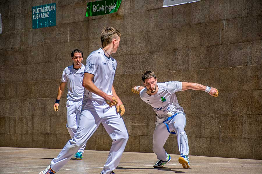 Ein Pilota-Spieler schlägt den Ball mit bloßer Hand, zwei weitere schauen zu ihm