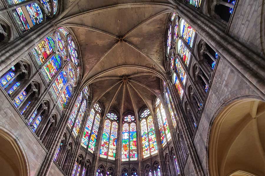 Blick von unten in einen gotischen Kirchenchor mit vielen bunten Fenstern